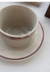 Close-up of minimalist silver heart studs on ceramic cup edge showing fine texture