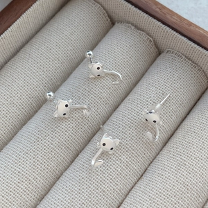 Boucles d'oreilles chat en argent S999 avec queue courbée sur un plateau à bijoux beige