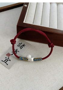 Macro shot of S999 silver fish pendant on a red braided bracelet with colorful silk details