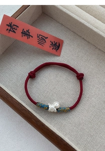 Detailed view of red woven rope bracelet with S999 silver ruyi charm on jewelry tray