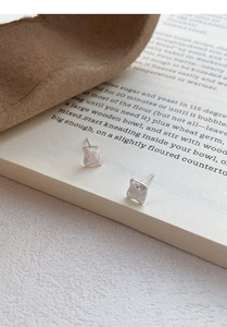 Macro shot of silver geometric square studs with a matte finish on a book background