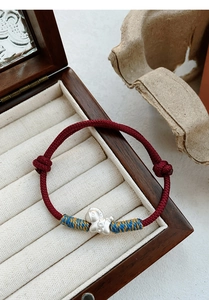 Detailed close-up of a braided red string bracelet with S999 silver astronaut charm detail