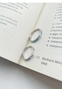 Détail de bagues de couple en argent S999 avec émail bleu sur les pages d'un vieux livre