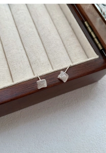 Macro detail of brushed S999 sterling silver square stud earrings on velvet jewelry box