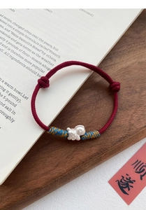 Detailed view of woven red string bracelet with silver fish charm and colorful thread detail