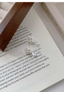 Macro detail of silver pearl flower earrings with a pear-cut zircon on vintage book pages