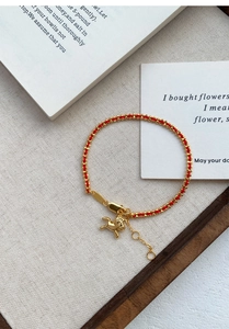 Détail d'un bracelet en corde tressée rouge avec pendentif poney doré et billes dorées
