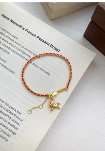 Détail du bracelet en corde rouge avec pendentif cheval doré et fermoir réglable sur livre