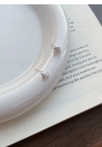 Minimalist square silver studs with brushed texture finish on a ceramic tray