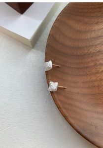 Macro detail of S925 sterling silver square stud earrings showing brushed metal texture