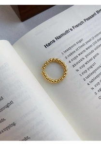 Détail d'une bague à perles dorées minimaliste posée sur des pages de livre