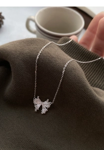 Detailed view of S999 silver bow necklace with pavé crystals on knitted fabric