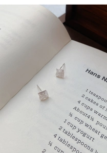 Macro detail of square matte silver stud earrings placed on an open book background