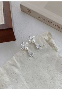 Detail of silver pearl flower earrings with water drop zircon on a beige canvas pouch