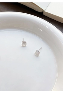 Macro shot of silver square stud earrings with matte brushed texture in a white ceramic dish