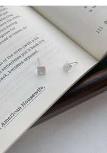 Macro detail of brushed S999 silver irregular square stud earrings on a book page