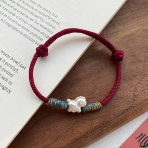 Handwoven red rope bracelet with a matte silver pig pendant on a wooden tray