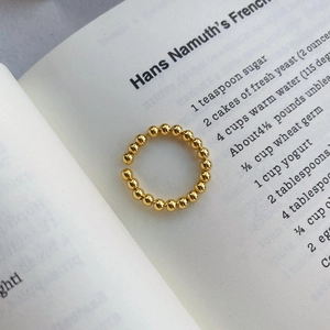 Bague perlée dorée ajustable en argent sterling poli posée sur un livre ancien