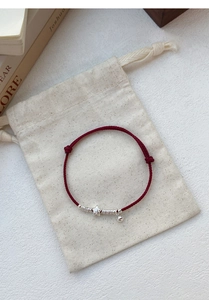 Detail of red woven rope bracelet with silver star charms on a beige linen pouch