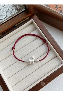 Macro view of S999 silver cartoon pig charm with coin patterns on red braided bracelet