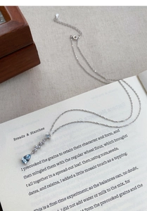 Detail of S925 silver necklace with blue teardrop zircon on a vintage book background