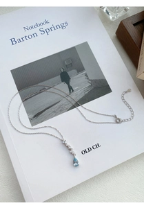 Macro shot of silver teardrop necklace with light blue zircon and dainty link chain