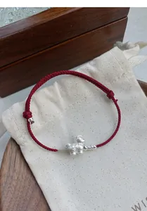 Detail of red braided silk bracelet featuring a silver zodiac sheep charm and coin motif