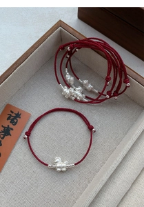 Close-up of a red braided rope bracelet with a silver pig charm in a wooden tray