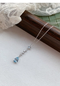 Macro view of blue teardrop zircon pendant on S999 silver chain with elegant lace background