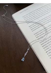 Detailed close-up of S999 silver necklace with blue teardrop zircon on an open book