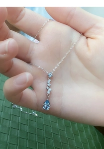 Close-up of S999 silver necklace with blue tear-shaped gemstone on green background