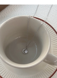 Dettaglio della collana a mezzaluna in argento S999 con zirconi in una tazza di ceramica