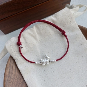 Red woven string bracelet with silver horse pendant on a beige linen gift pouch