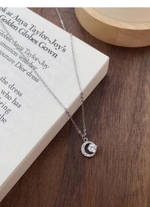 Vista macro di una collana a mezzaluna in argento S999 con zirconi su un libro