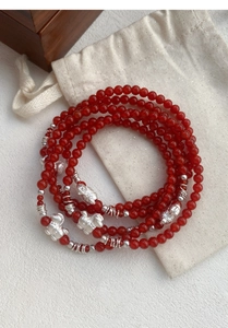 Dettaglio macro di perle di agata rossa e ciondoli Pixiu in argento su bracciale multiplo
