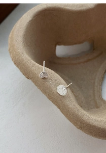 Macro detail of asymmetric silver rose and circular relief earrings on textured paper