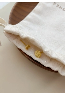 Detail view of golden rose and coin earrings on a textured fabric pouch and wooden tray