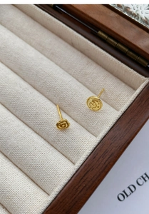 Detailed macro shot of gold asymmetric rose and prince engraved stud earrings on beige velvet