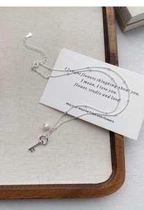 Macro shot of S925 sterling silver key necklace with small pearl on wooden display board