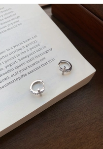 Close-up of S925 sterling silver hoop earrings with diamond-set cross charms on a book