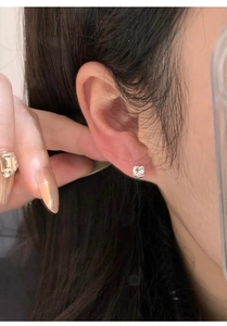 Detailed view of an Asian model wearing a delicate silver heart-shaped zircon stud earring