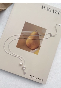 Detail of S925 sterling silver key necklace with freshwater pearl on a magazine