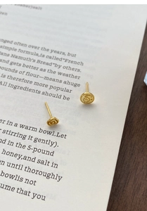 Macro detail of gold S999 silver earrings featuring coin relief and rose motifs on book