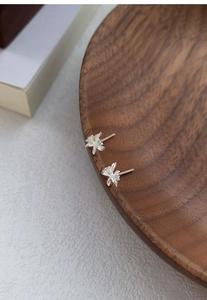 Dettaglio di orecchini a lobo orchidea in argento S999 con zirconi su vassoio in legno