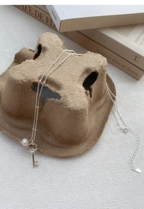 Close-up of S925 sterling silver key necklace with pearl on vintage books background