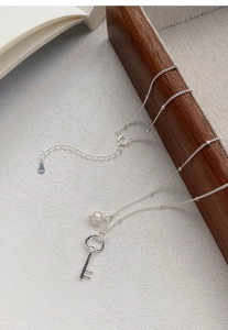 Detailed close-up of S925 silver key necklace with a freshwater pearl on a textured background