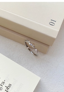Macro detail of silver wheat leaf ring with sparkling zircons against a warm background