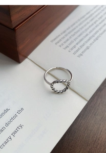 Gros plan sur une bague torsadée argentée posée sur des pages de livre et du bois