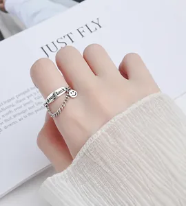 Primer plano del anillo de plata S999 con placa 'Good Luck' y colgante de smiley