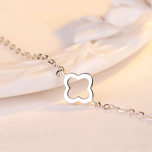 Macro shot of silver hollow clover charm with delicate cross chain on ceramic background